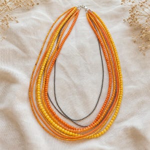 Gift ready presentation of Long multistrand orange amber yellow and gunmetal necklace in an open jewelry box lined with natural ivory linen