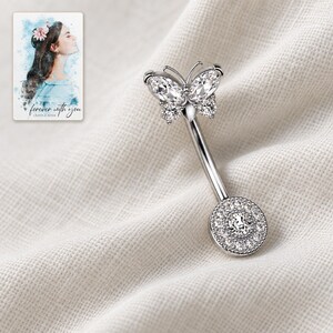 The single clear-stone style butterfly navel bar lies diagonally on folded ivory linen. A personalized digital greeting card is shown alongside.