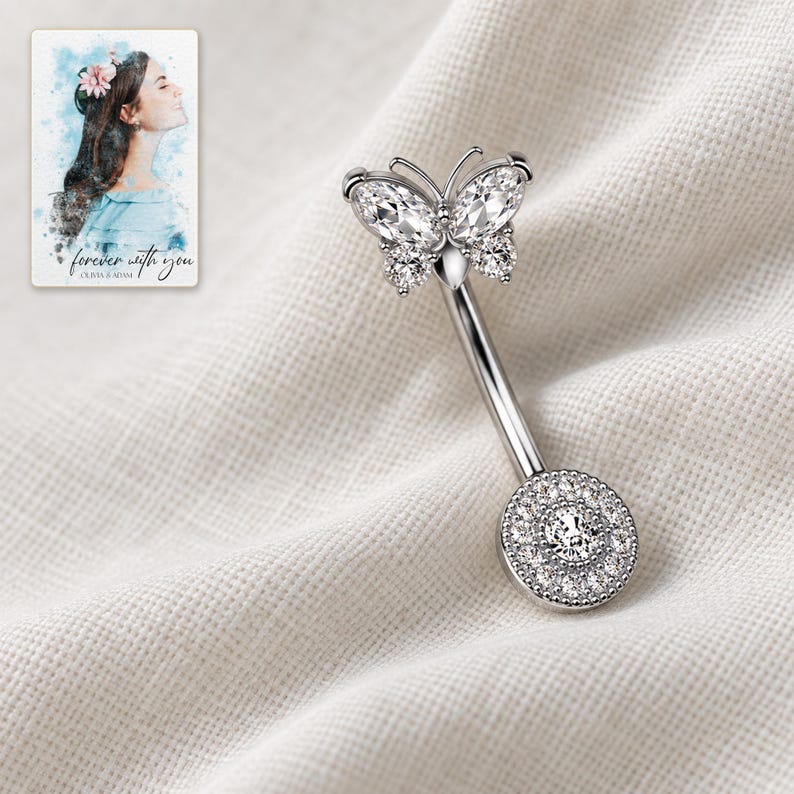 The single clear-stone style butterfly navel bar lies diagonally on folded ivory linen. A personalized digital greeting card is shown alongside.