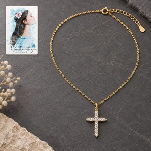 Golden cross necklace styled on matte charcoal stone style with controlled reflections and clear stone style detail. A personalized digital greeting card is shown alongside.