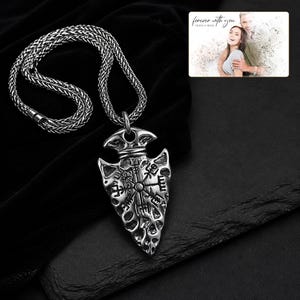 May include: A silver-toned arrowhead pendant featuring an engraved Vegvisir symbol on a thick woven chain. Included is a rectangular card displaying a photograph of a couple with the text "forever with you" and "OLIVIA & ADAM" printed at the top.