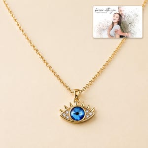 Gold-tone necklace with a blue eye-shaped pendant, display view. A personalized greeting-card example appears in the corner.