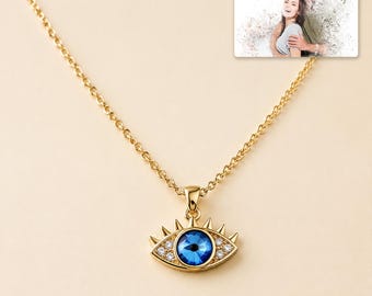 May include: A gold-tone chain necklace featuring an evil eye pendant with a central blue crystal, surrounded by small clear stones and gold spikes. A rectangular card displays a photo of a couple with the text "forever with you" and "OLIVIA & ADAM".