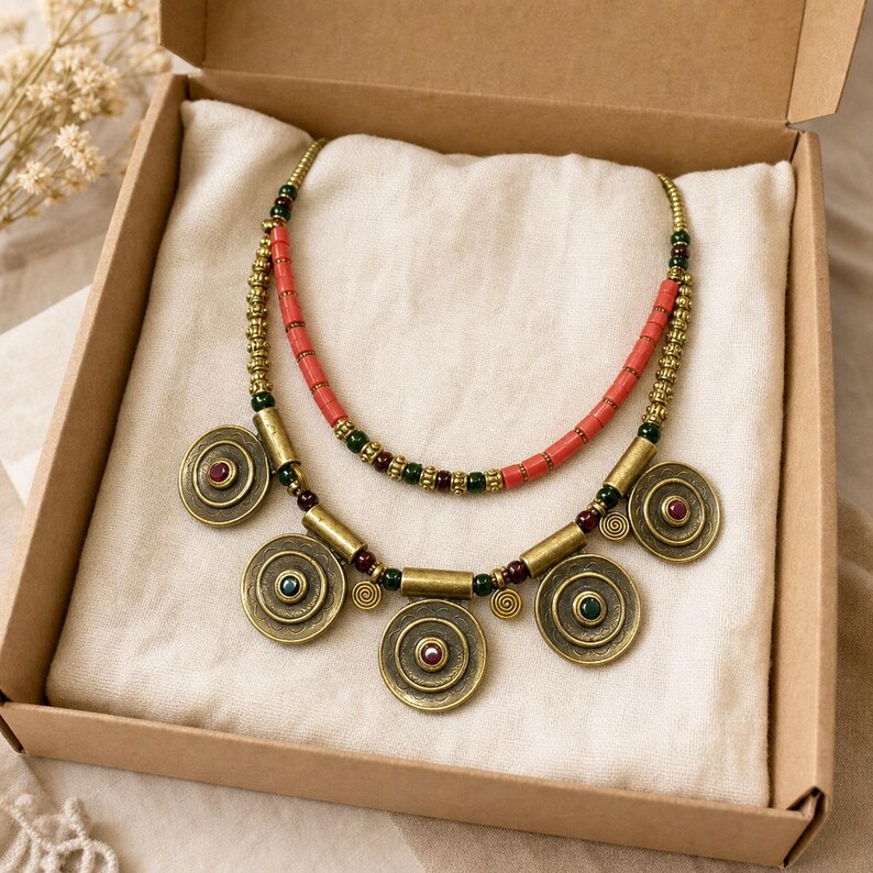Two-strand coral and antique-brass necklace with five spiral medallions worn with an ivory linen top in warm natural window light