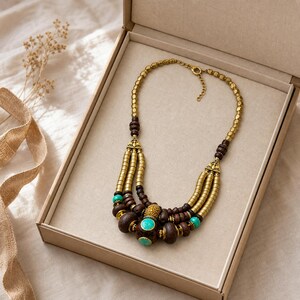 Peut inclure: Un collier imposant &agrave; plusieurs rangs compos&eacute; de perles en bois brun fonc&eacute;, de perles cylindriques dor&eacute;es m&eacute;talliques et d'accents turquoise vif. Le collier comprend un fermoir en m&eacute;tal dor&eacute; et une courte cha&icirc;nette d'extension, pr&eacute;sent&eacute; en bo&icirc;te.