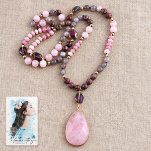 The Pink option bead necklace on folded natural linen, with its teardrop pendant and purple accents clearly visible. A personalized digital greeting card is shown alongside.