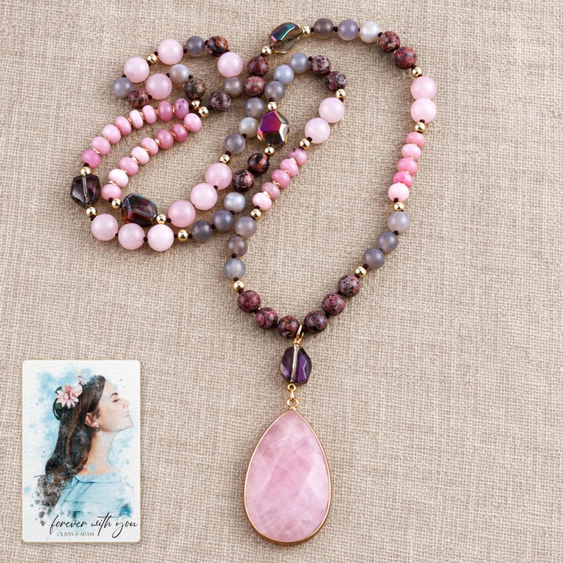 The Pink option bead necklace on folded natural linen, with its teardrop pendant and purple accents clearly visible. A personalized digital greeting card is shown alongside.