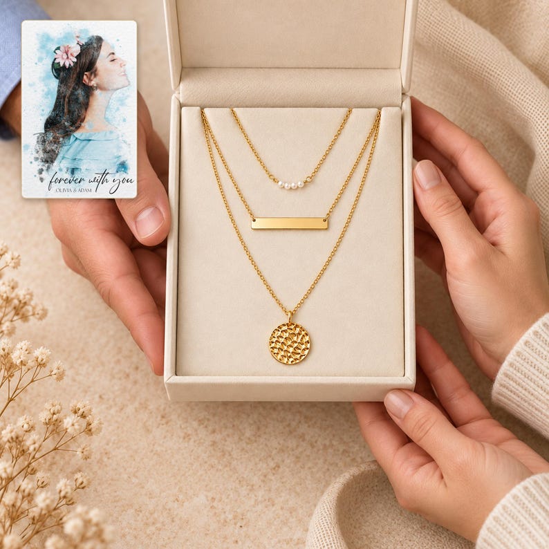 Two adults exchanging an open box with all three necklaces visible: a small pearl-style beads cluster, wide bar and textured coin. A personalized digital greeting card is shown alongside.