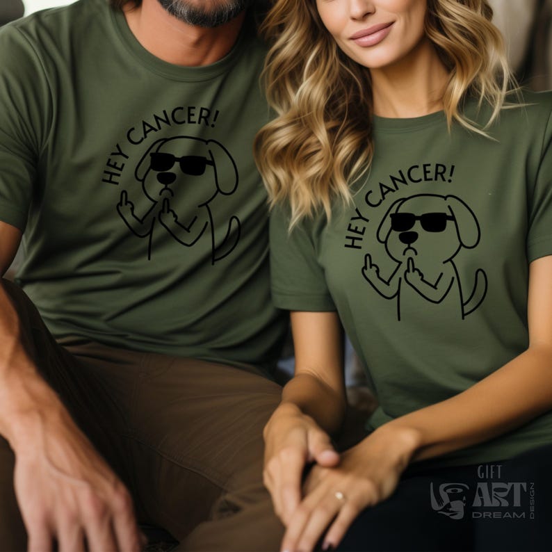 May include: Two people wearing matching green t-shirts with a black cartoon dog wearing sunglasses and giving the middle finger. The text on the shirts says "Hey Cancer!"