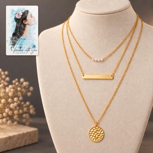 Gold-tone three-necklace set displayed against dark graphite, with four white pearl-style beads and a textured coin clearly visible. A personalized digital greeting card is shown alongside.