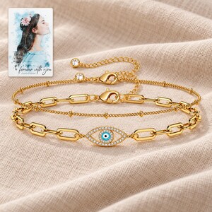 Gold Tone Evil Eye Bracelet Duo arranged on soft ivory linen in a refined neutral flat lay. A personalized digital greeting card is shown alongside.