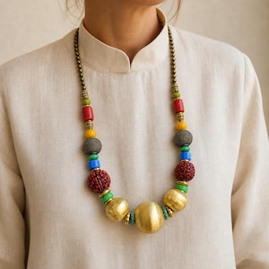 Bold multicolor carved bead and brushed gold sphere necklace worn with an ivory linen top in warm natural window light