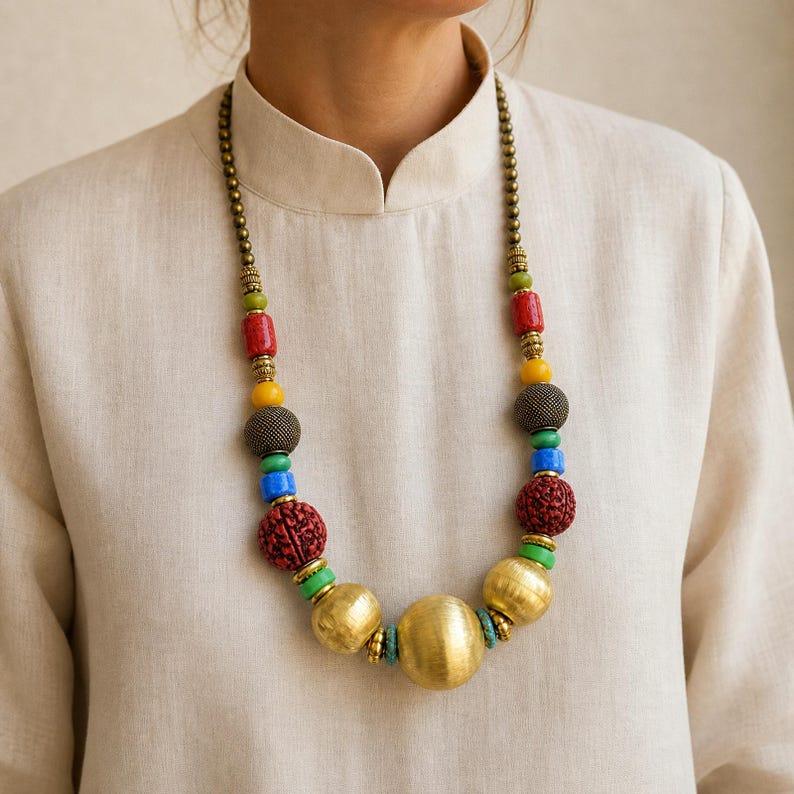 Bold multicolor carved bead and brushed gold sphere necklace worn with an ivory linen top in warm natural window light