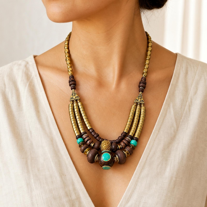 Antique-brass and brown statement necklace displayed on a jewelry bust with all three brass-bead strands and the turquoise-inlaid focal bead visible