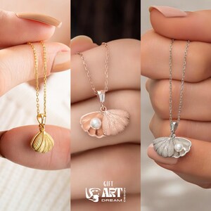 Op de afbeelding: Drie kettingen met schelpenhangers in goud, ros&eacute;goud en zilver. Elke ketting heeft een delicate ketting en een hanger in de vorm van een schelp, met een klein parelaccent. De afbeelding bevat de tekst "GIFT ART DREAM DESIGN".