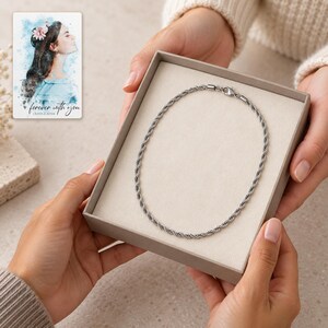 An adult offers an open taupe styling box containing a single silver-tone rope necklace. A personalized digital greeting card is shown alongside.