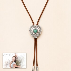 Brown cord bolo necklace with a silver-tone heart slide and turquoise-color center, close detail view. A personalized greeting-card example appears in the corner.