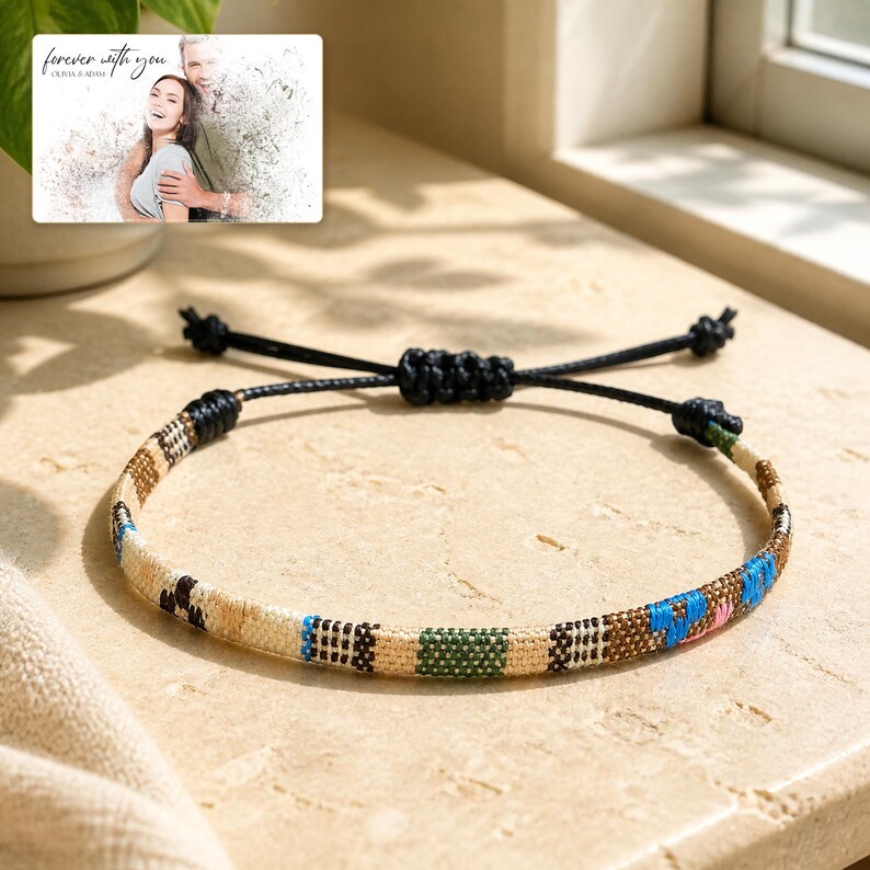 May include: A woven bracelet featuring a geometric pattern in beige, black, green, and blue threads with an adjustable black cord closure. Above the bracelet, a rectangular card displays a photo of a couple with the text "forever with you".