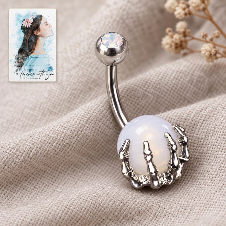 Silver-tone skeleton-claw barbell resting on folded oatmeal linen in soft window light. A personalized digital greeting card is shown alongside.