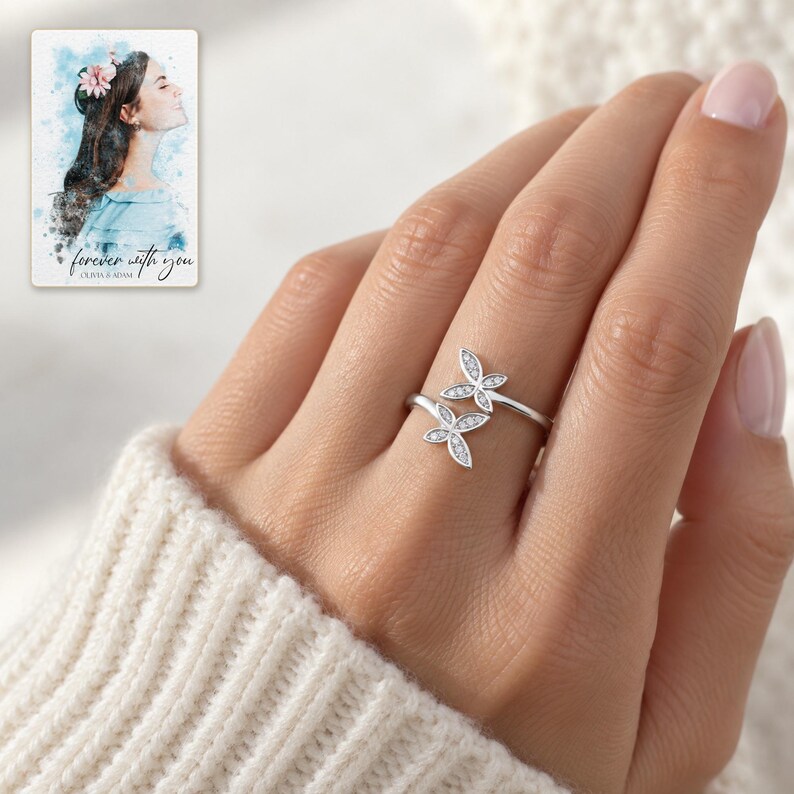 Adult woman wearing the double butterfly silver-tone ring with a cream knit sleeve in daylight. A personalized digital greeting card is shown alongside.
