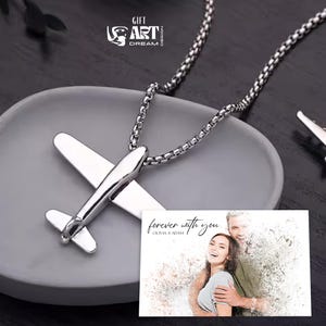 Może przedstawiać: Srebrny naszyjnik z zawieszką w kształcie samolotu i łańcuszkiem. Naszyjnik jest prezentowany na szarej misce, z kartą z napisem "forever with you" i imionami Olivia & Adam.