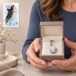 Fully clothed adult woman presents a small open taupe box containing the white-ball skeleton-claw barbell. A personalized digital greeting card is shown alongside.