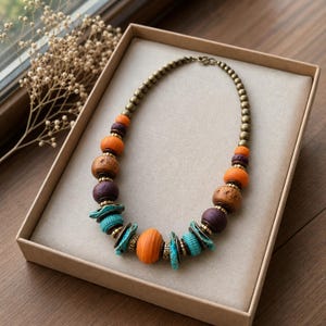 Antique gold tone burnt orange plum and turquoise statement bead necklace worn with an ivory linen top in warm natural window light