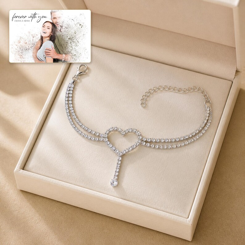 May include: A silver-toned bracelet featuring a double-strand chain of clear crystals, a central heart-shaped charm, and a dangling crystal accent. Included is a rectangular card with a photograph of a couple and the text "forever with you".