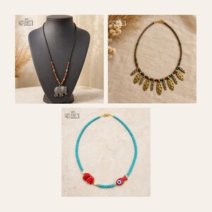 May include: Three necklaces: one with a silver elephant pendant on a beaded cord, one with gold-toned textured leaf-shaped charms and multi-colored beads, and one with turquoise beads, red coral-like segments, and a red fish-shaped charm.