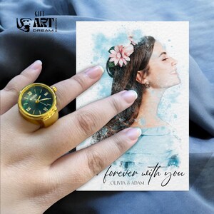 Peut inclure: Une bague-montre dor&eacute;e avec un cadran vert et des chiffres romains. La bague est sur une main &agrave; c&ocirc;t&eacute; d'une carte aquarelle avec un portrait de femme et le texte "forever with you, Olivia & Adam."