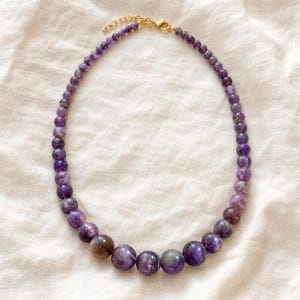 Gift ready presentation of Single-strand graduated marbled purple bead necklace with gold-tone lobster clasp in an open jewelry box lined with natural ivory linen