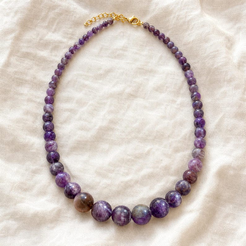 Gift ready presentation of Single-strand graduated marbled purple bead necklace with gold-tone lobster clasp in an open jewelry box lined with natural ivory linen