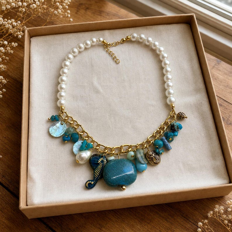 White pearl teal blue stone and fish charm statement necklace worn with an ivory linen top in warm natural window light
