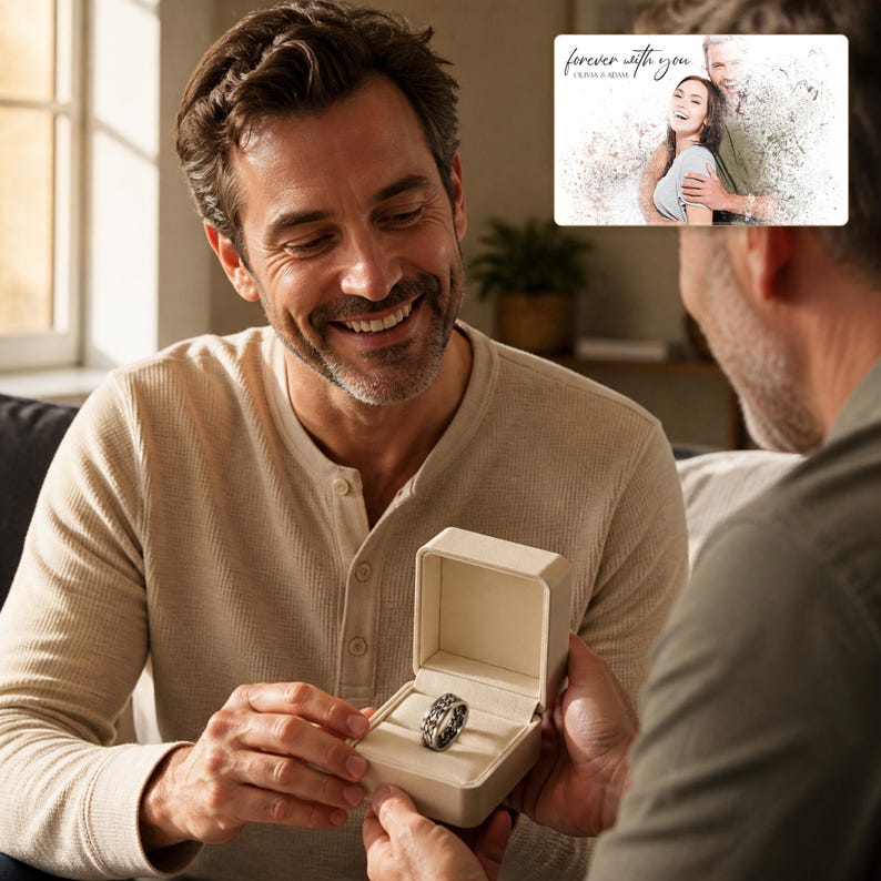 May include: A silver-toned metal ring with an intricate, textured pattern sits inside a small, open, cream-coloured rectangular jewellery box. The ring features a repeating design around its entire band, presented in a clean, neutral-coloured case.