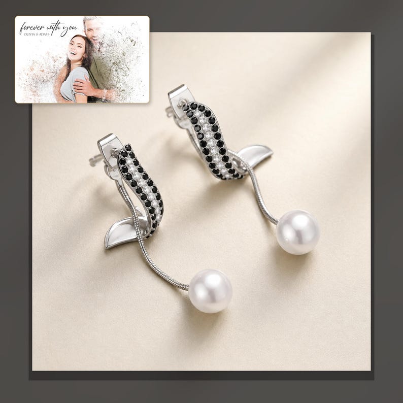 Silver-tone curved drop earrings with black accents and white round drops, dark-bordered product view. A personalized greeting-card example appears in the corner.