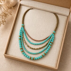 May include: A multi-strand necklace featuring turquoise-colored beads, metallic bronze-toned beads, and small gold-toned spacers. The design consists of five cascading layers of beads arranged in a curved, semi-circular shape within a box.