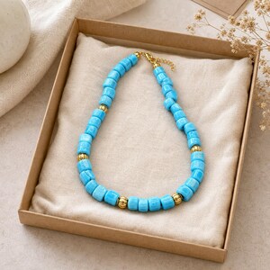 Top down lifestyle view of Chunky turquoise rectangular-bead necklace with antique-gold spacers on softly textured ivory linen