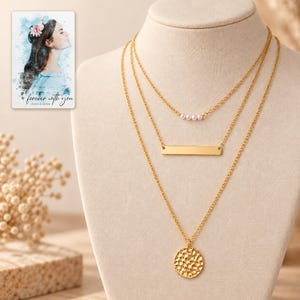 Complete pearl-style beads, bar and hammered coin necklace trio on an ivory display against a warm neutral background. A personalized digital greeting card is shown alongside.