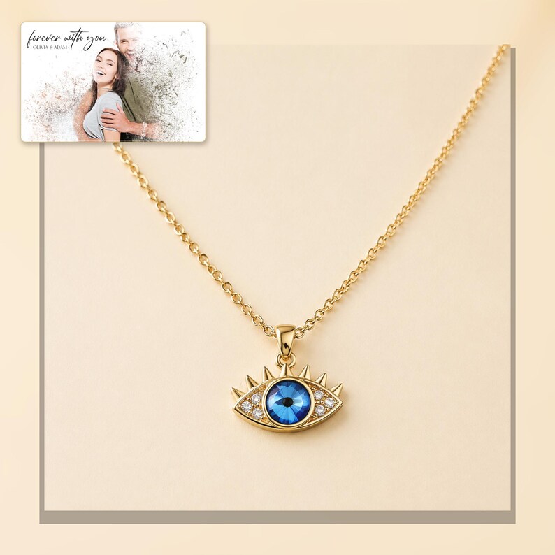 Gold-tone necklace with a blue eye-shaped pendant, light-bordered product view. A personalized greeting-card example appears in the corner.