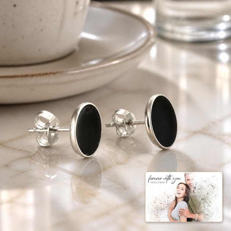 Black oval stud earrings with silver-tone edges, adult lifestyle view. A personalized greeting-card example appears in the corner.