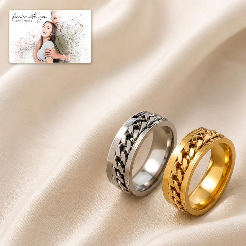 May include: Two spinner rings, one silver-toned and one gold-toned, each featuring a central rotating chain link band. A small rectangular card is visible in the upper left corner displaying a photograph of a couple with the text forever with you.