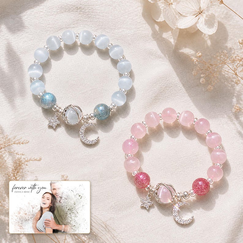 Puede incluir: Dos pulseras de cuentas con perlas ojo de gato en azul claro y rosa, espaciadores plateados y dijes en forma de estrella, luna creciente y planeta. Una peque&ntilde;a tarjeta rectangular muestra el texto "forever with you OLIVA & ADAM".