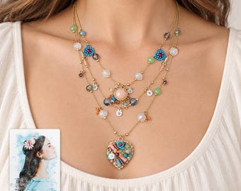May include: A multi-strand gold-tone necklace featuring various colorful beads, small flower charms, and a central heart-shaped pendant filled with assorted stones. A small card is visible with a watercolor illustration and the text "forever with you".