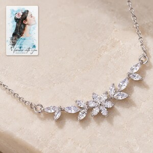 Close view of the silver-tone necklace's single six-petal flower and clear marquise leaf branches. A personalized digital greeting card is shown alongside.