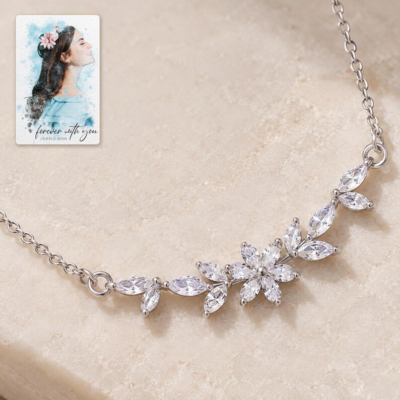Close view of the silver-tone necklace's single six-petal flower and clear marquise leaf branches. A personalized digital greeting card is shown alongside.