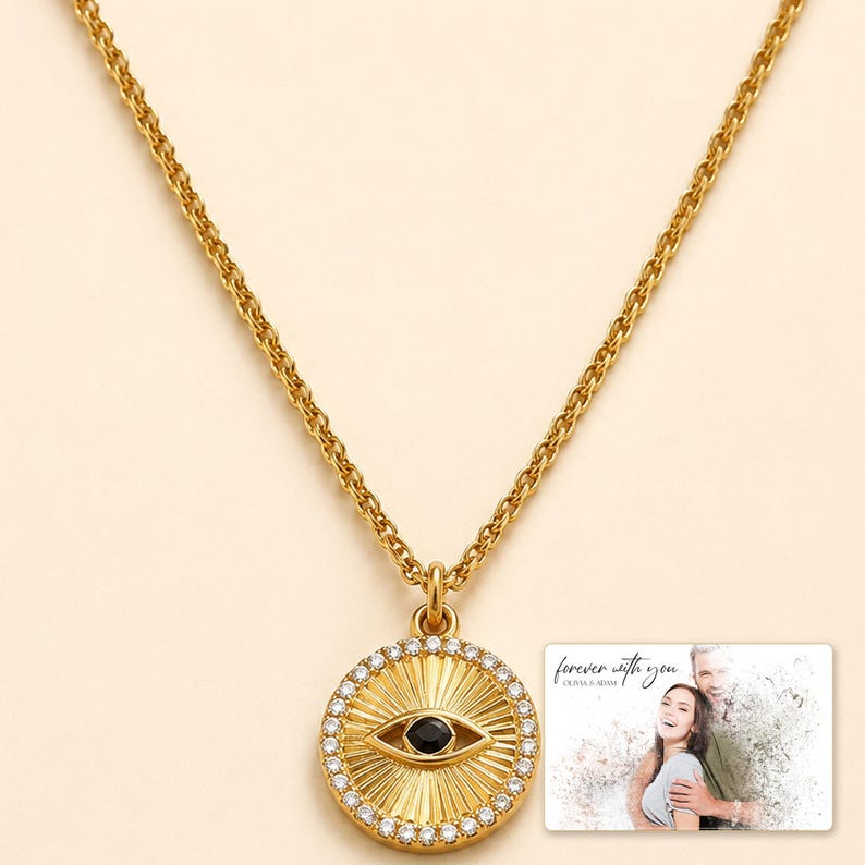 Gold-tone necklace with a round sunburst and black eye detail, close detail view. A personalized greeting-card example appears in the corner.