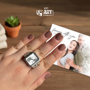 May include: A silver ring watch with a square face is worn on a finger. The watch has a white dial with black hands and Roman numeral hour markers. The image also shows a card with the words "forever with you". The logo "GIFT ART DREAM DESIGN" is also visible.