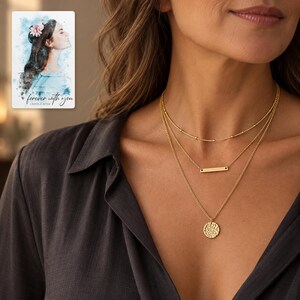 Adult woman wearing the satellite, bar and hammered coin necklace with a charcoal blouse in soft evening light. A personalized digital greeting card is shown alongside.