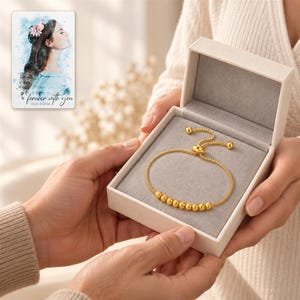 Golden Spiral Bead Slider Bracelet shown during a believable gift-giving moment between adults with the jewelry visible. A personalized digital greeting card is shown alongside.