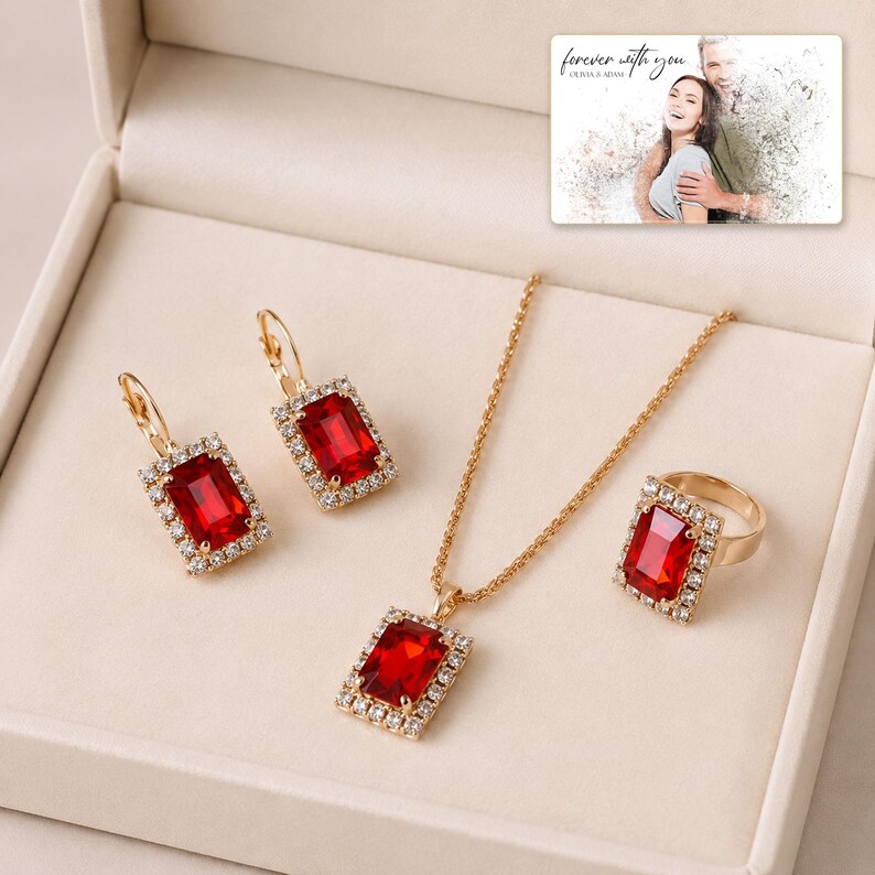 Red rectangular-stone necklace, matching earrings and ring, presentation in an open jewelry box. A personalized greeting-card example appears in the corner.